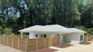 A small, single-story building with a sloped roof, a covered porch, and a fenced area. - Florida style  built  2023. Heated pool. Dog park. 10 min walk to beach.  (Southern Shores)