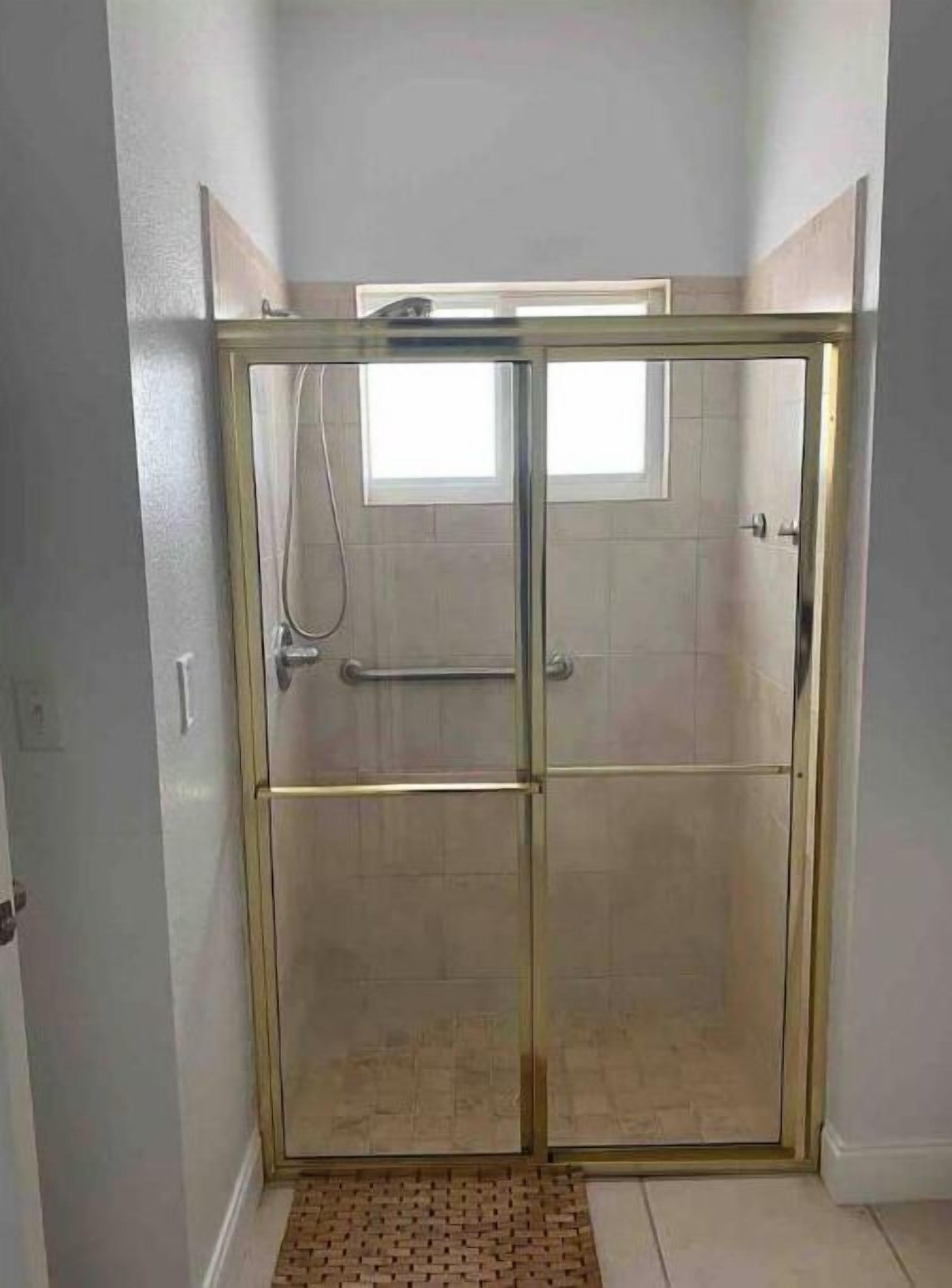 A glass-enclosed shower area with a tiled floor and a small window above the door.
