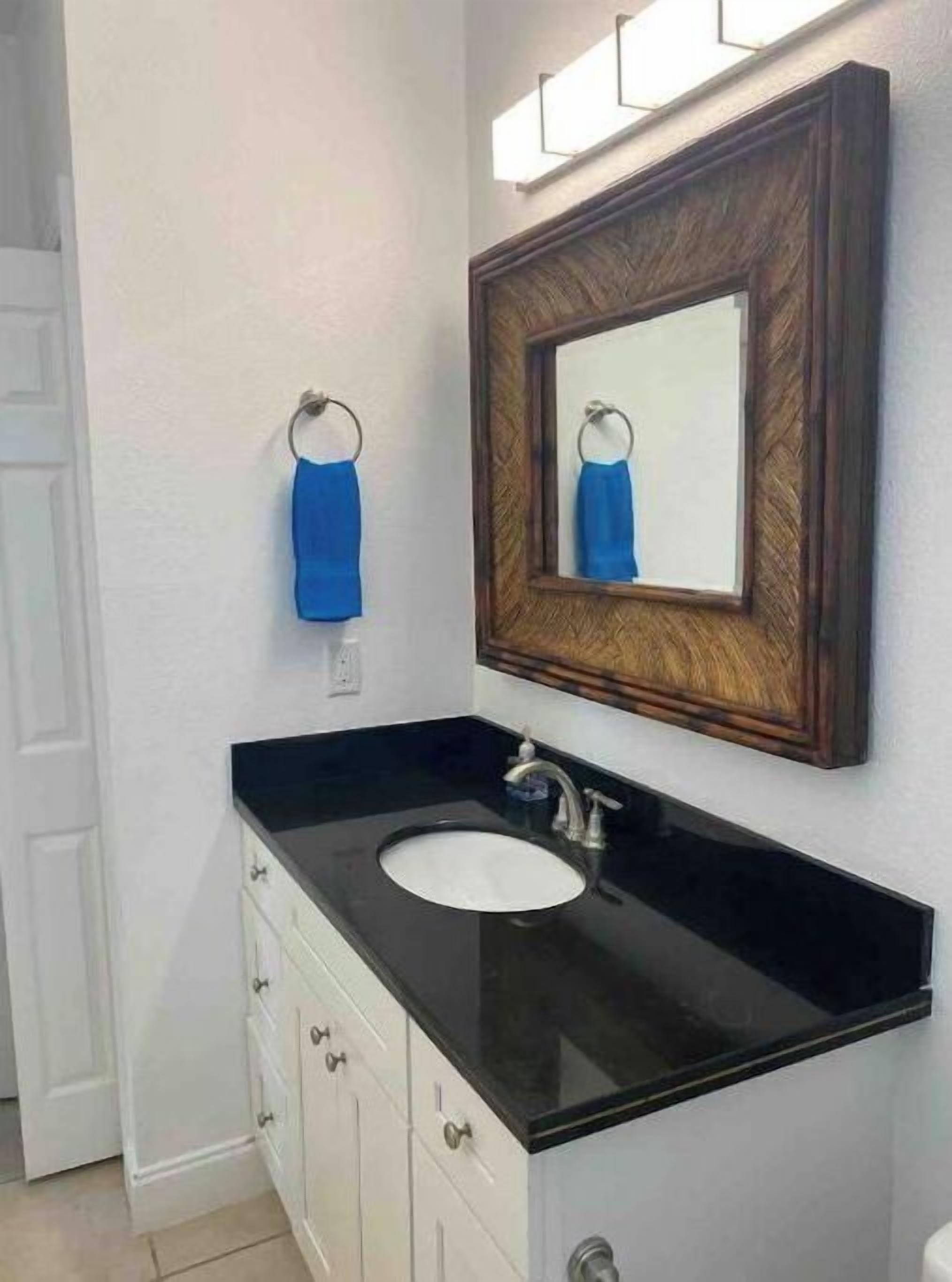 A bathroom with a black countertop sink, a wooden-framed mirror, and a blue towel hanging on a metal ring.