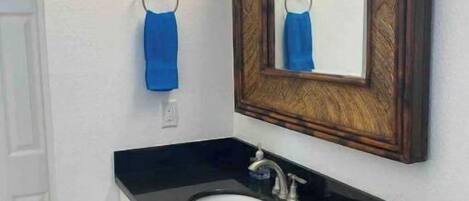 A bathroom with a black countertop sink, a wooden-framed mirror, and a blue towel hanging on a metal ring.