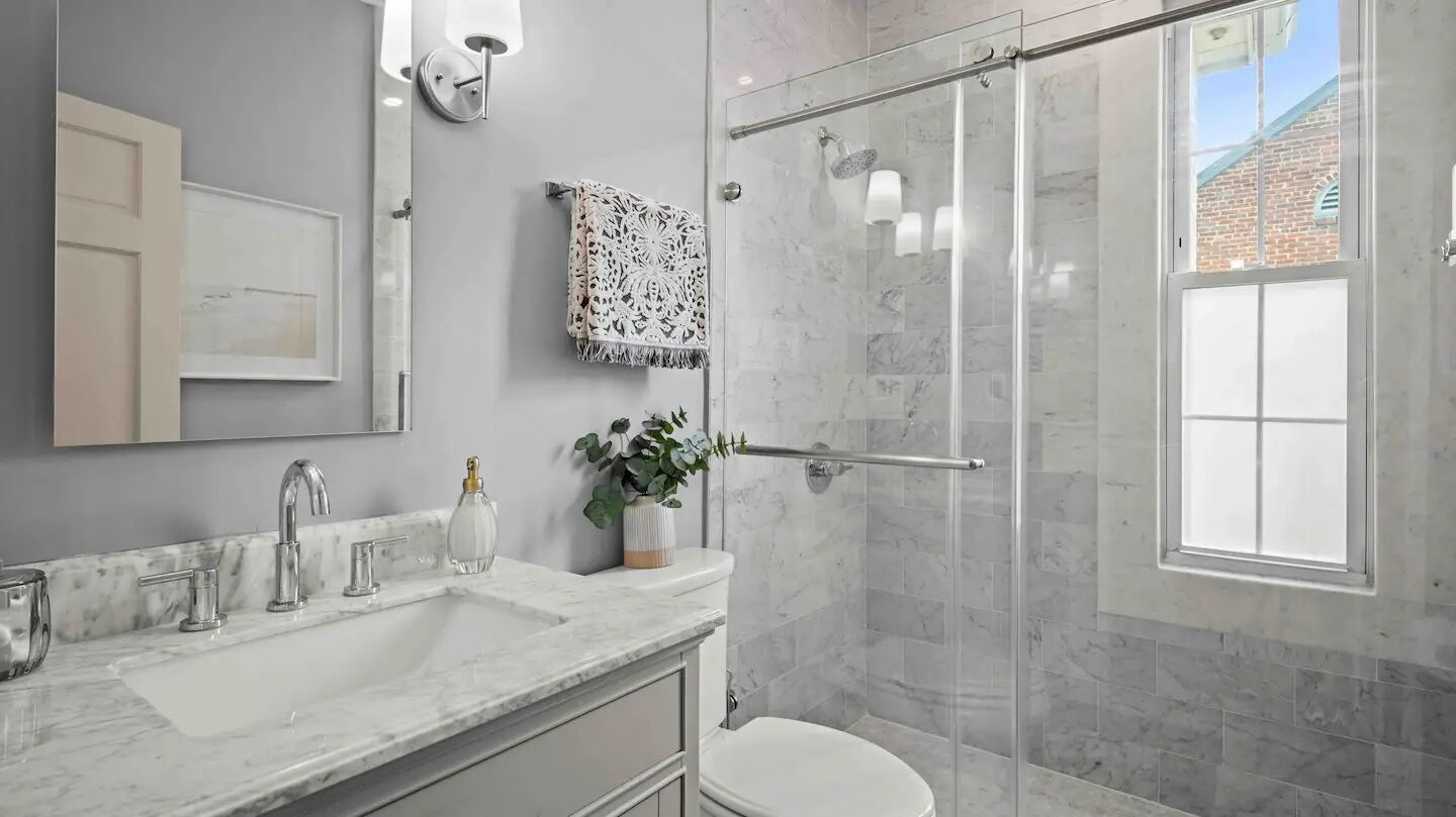 A modern bathroom with a glass shower enclosure, a large sink with a mirror, and a toilet.