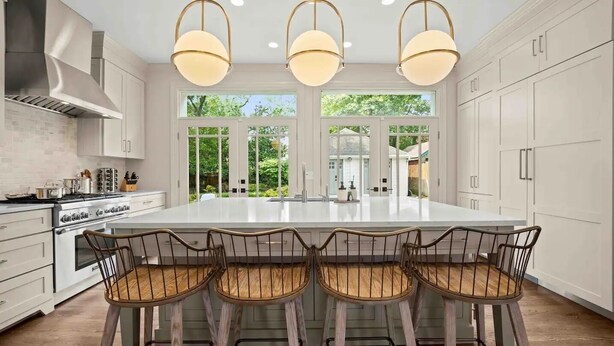 A modern kitchen with a large island, white cabinetry, and a view of greenery outside.