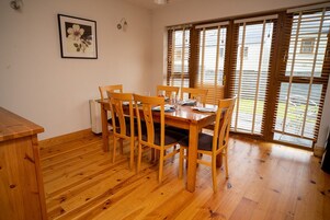 Un comedor con una mesa y sillas de madera, un cuadro en la pared y ventanas amplias con persianas.