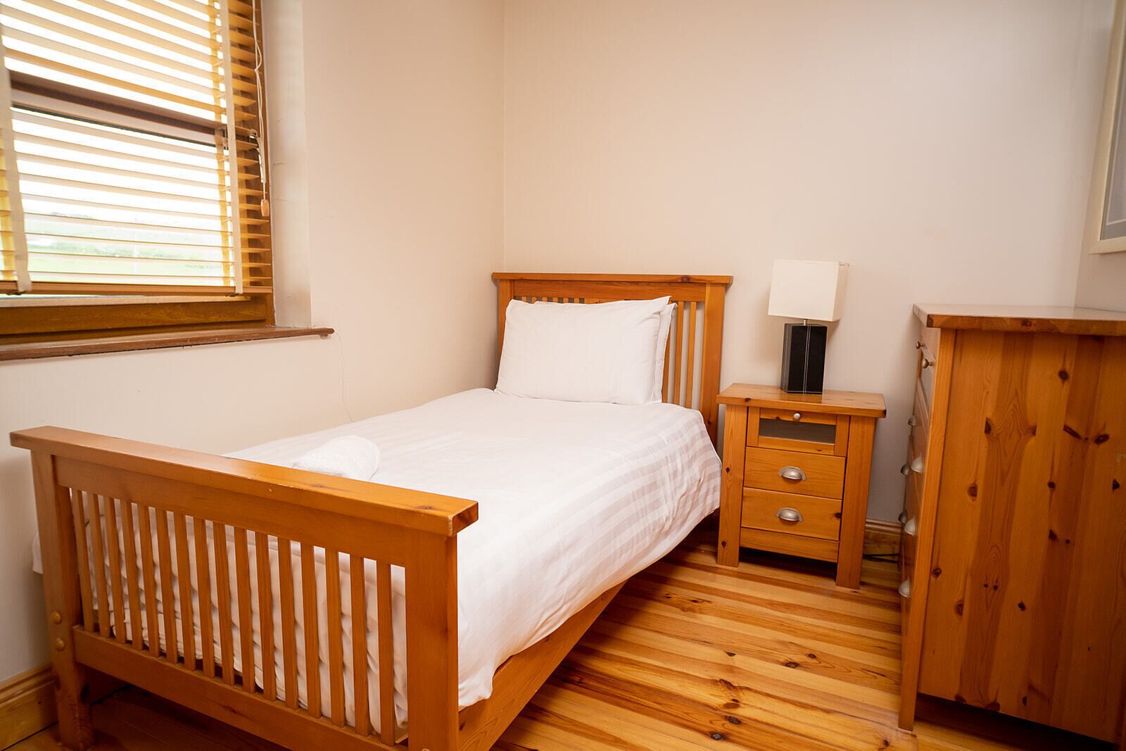 A bedroom with a wooden bed, a bedside table with drawers, a nightstand, and a wardrobe.