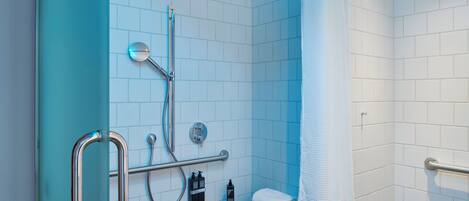 A modern bathroom with a glass shower enclosure, a handrail, a towel rack, and a toilet.