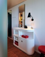 Un baño moderno con tocador blanco, un espejo, una lámpara negra en la pared y un banco rojo.