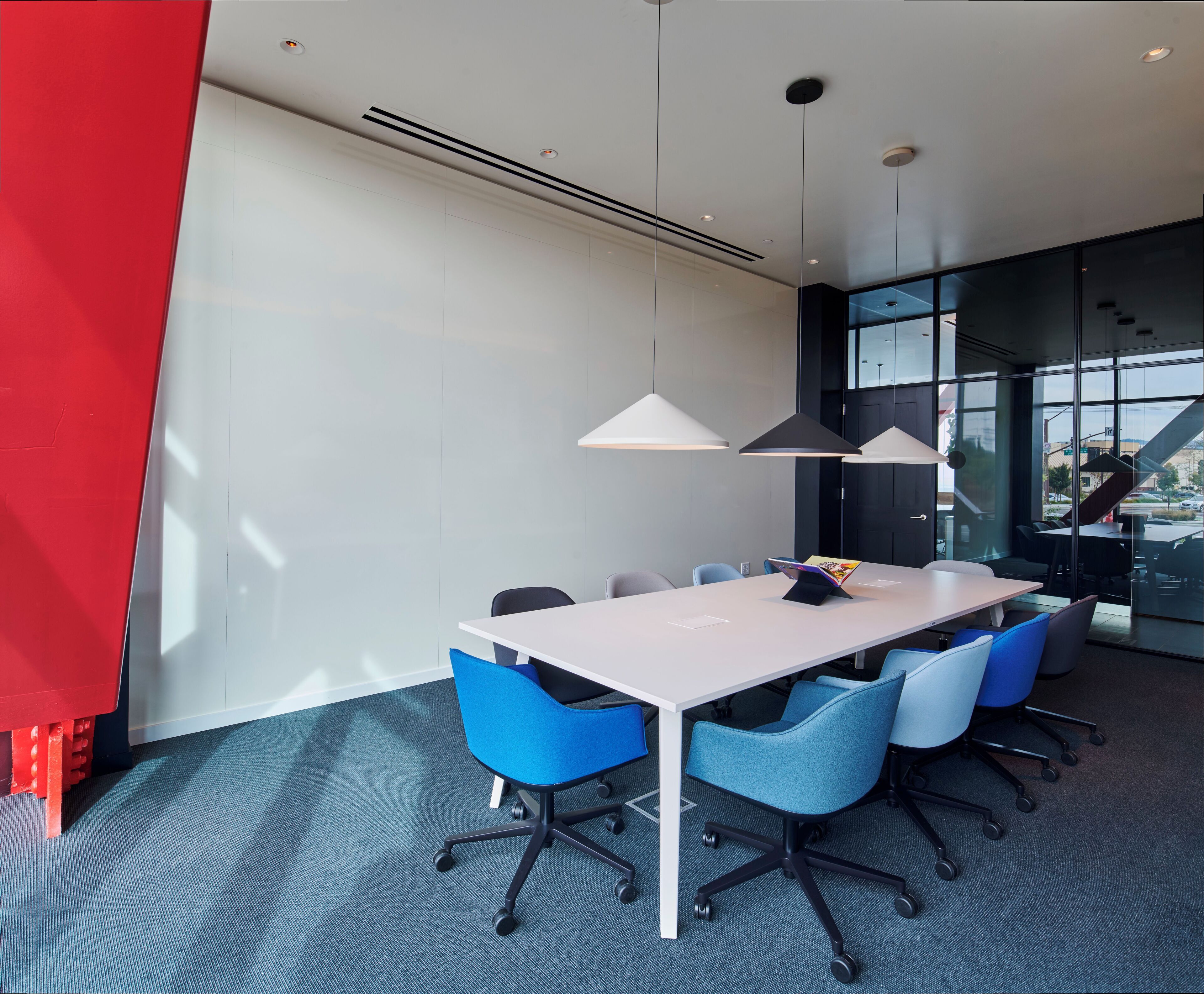 A modern conference room with a white table, blue chairs, and pendant lighting.