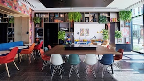 A modern dining area with a long wooden table, colorful chairs, and a variety of plants and decorations. - citizenM Menlo Park (Menlo Park)