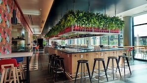 A modern bar area with a central island, bar stools, and a ceiling with hanging plants. - citizenM Menlo Park (Menlo Park)