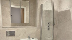 Un baño moderno con ducha de vidrio, lavamanos pedestal y inodoro.