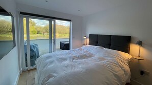 Un dormitorio con una cama grande, un ventanal corredero que da a un balcón y una mesita de noche con lámpara.