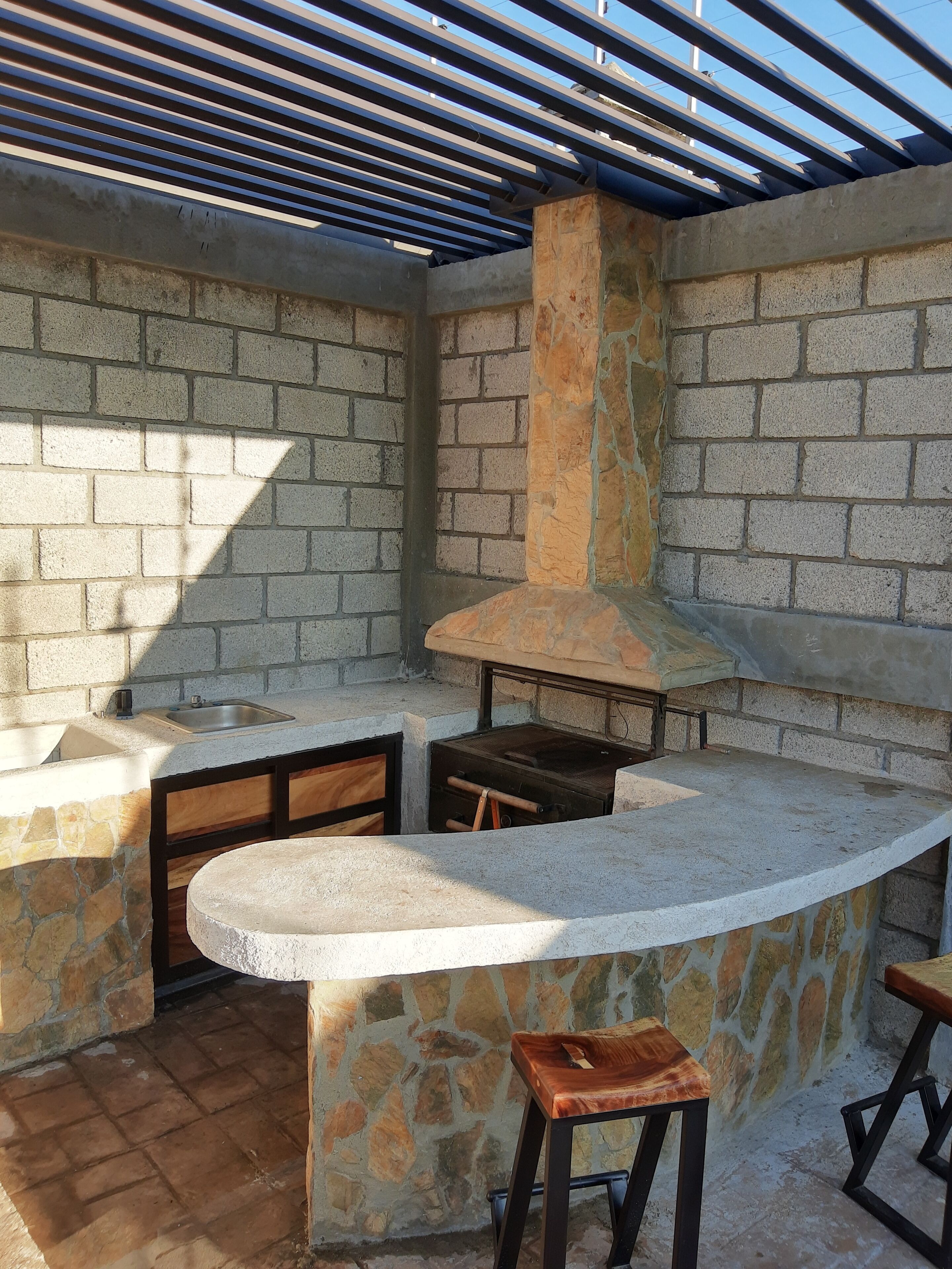 An outdoor kitchen area with a stone counter, a built-in grill, and a wooden stool.
