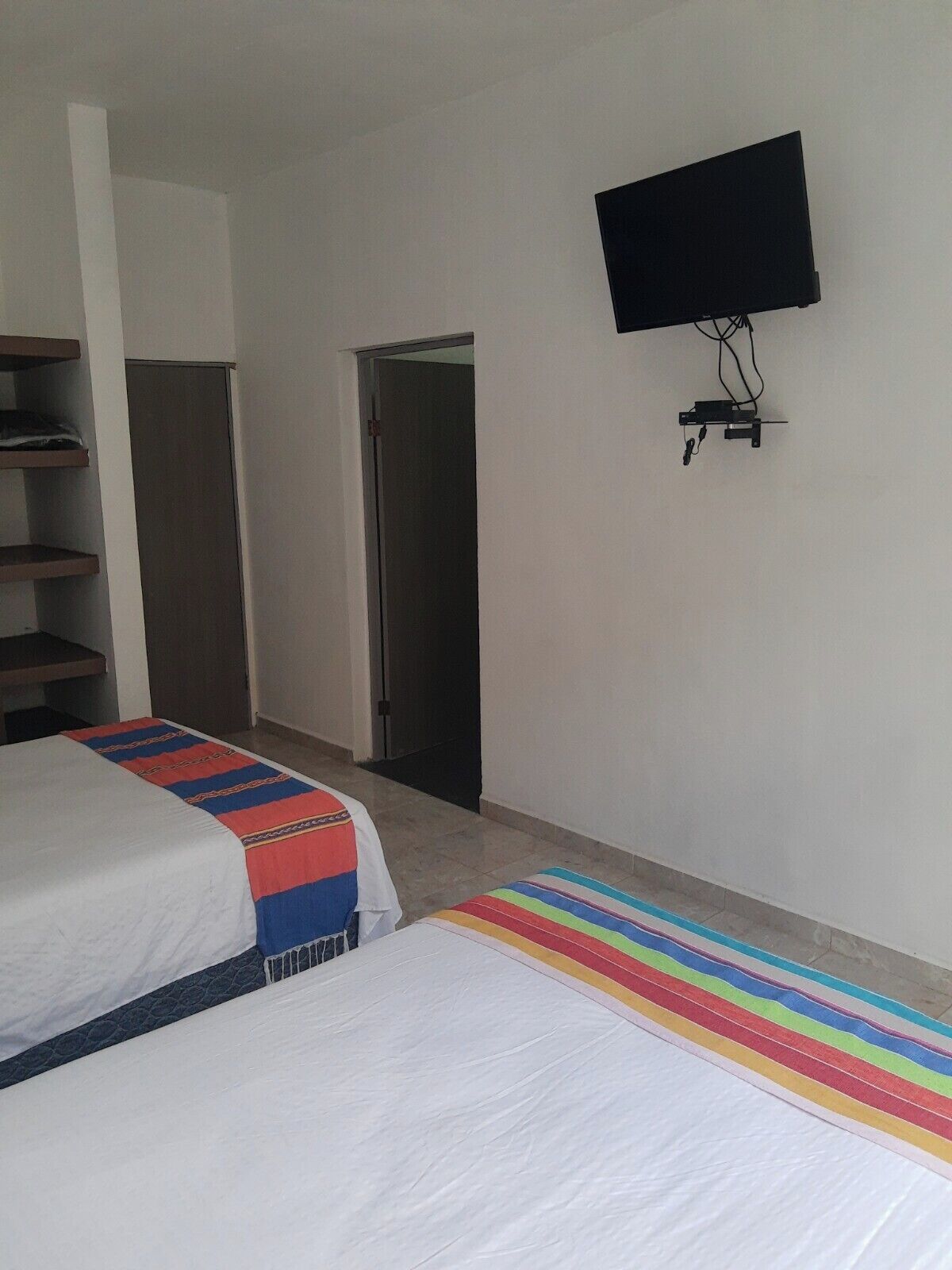 A hotel room with two beds, a TV mounted on the wall, and a door leading to another room.