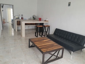 A modern living room with a black sofa, wooden coffee table, and a kitchen area with a microwave, sink, and stools. - Hotel Boutique Alebrijes Salina Cruz (Salina Cruz)