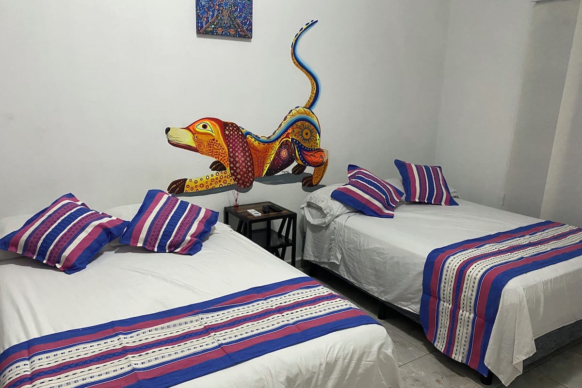Une chambre d’hôtel avec deux lits, chacun agrémenté de draps à rayures et d’oreillers assortis. Une sculpture colorée représentant un singe est accrochée au mur, au-dessus des lits.