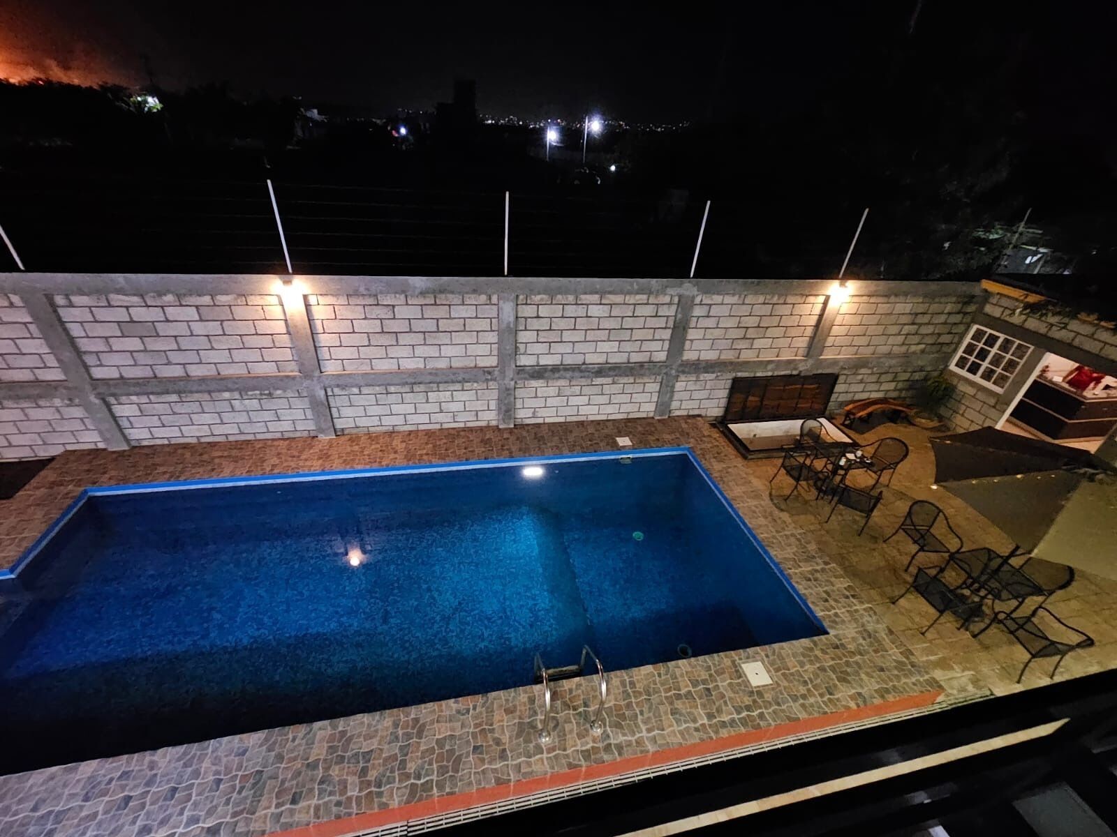 Una piscina exterior con un muro de ladrillo y un patio amueblado con sillas y una mesa.