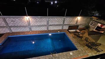 Una piscina exterior con un muro de ladrillo y un patio amueblado con sillas y una mesa.