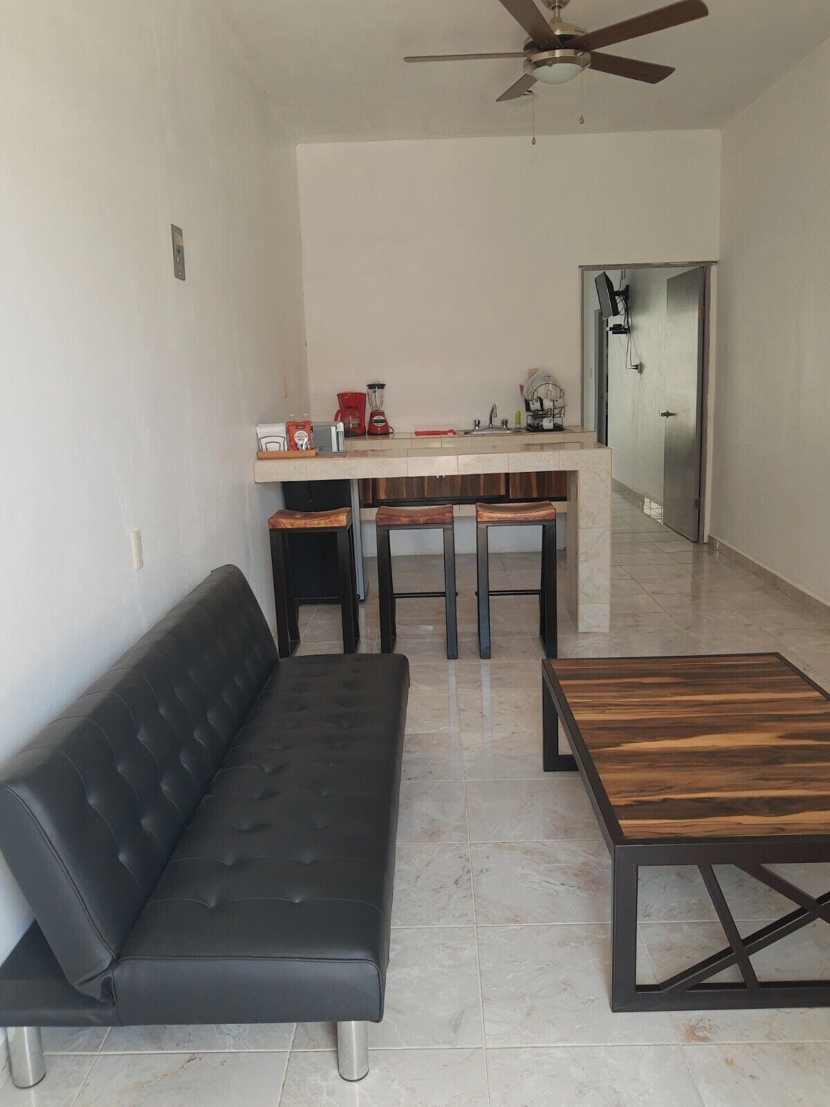 A modern living room with a black sofa, a wooden coffee table, and a kitchen area with a countertop and stools.
