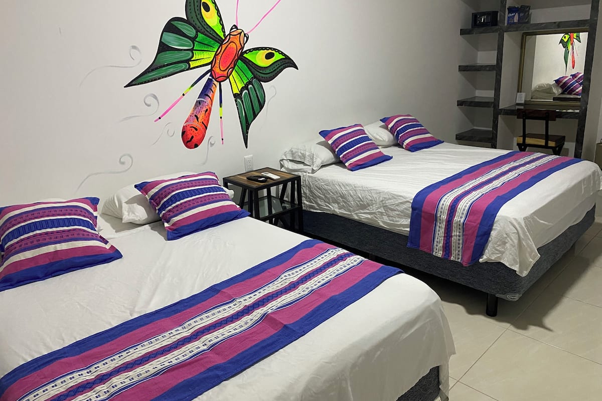 Une chambre d’hôtel avec deux lits, chacun agrémenté de draps à rayures, une fresque murale représentant un papillon et une petite table avec une télécommande.