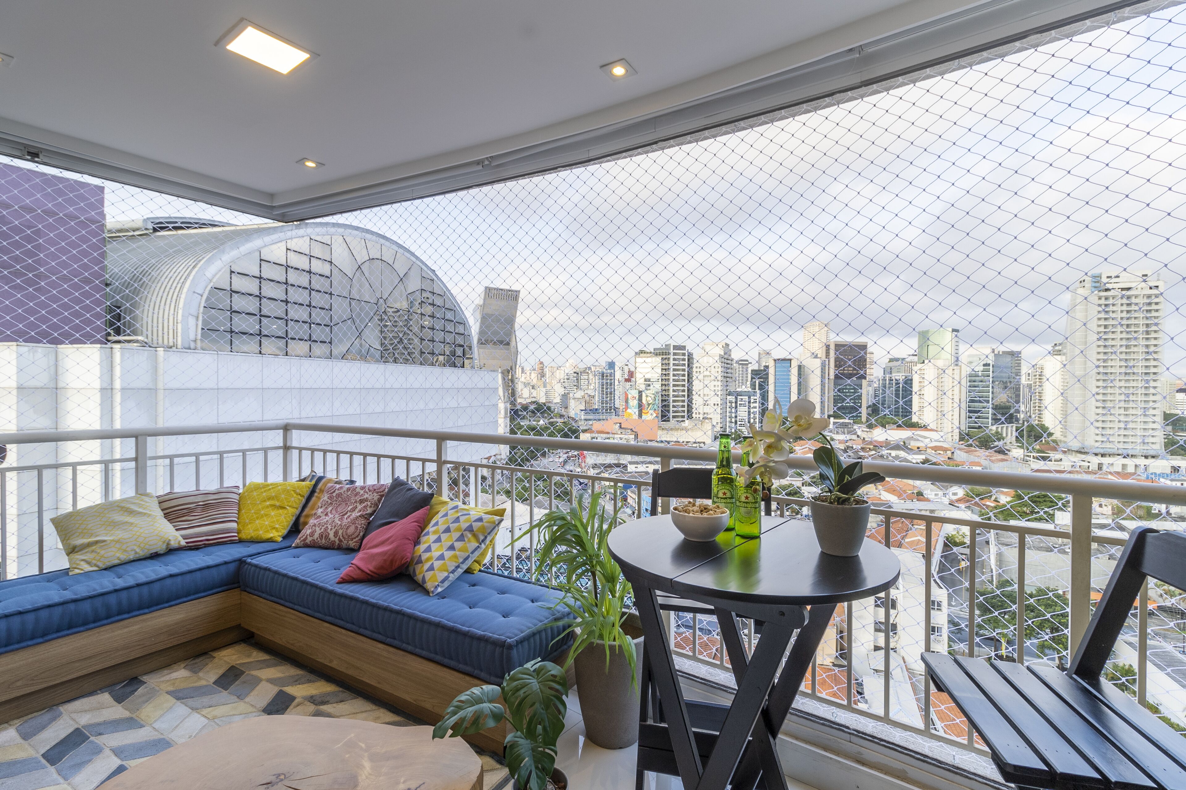 En balkon med en blå sofa, et lille bord med en plante og udsigt over byen.