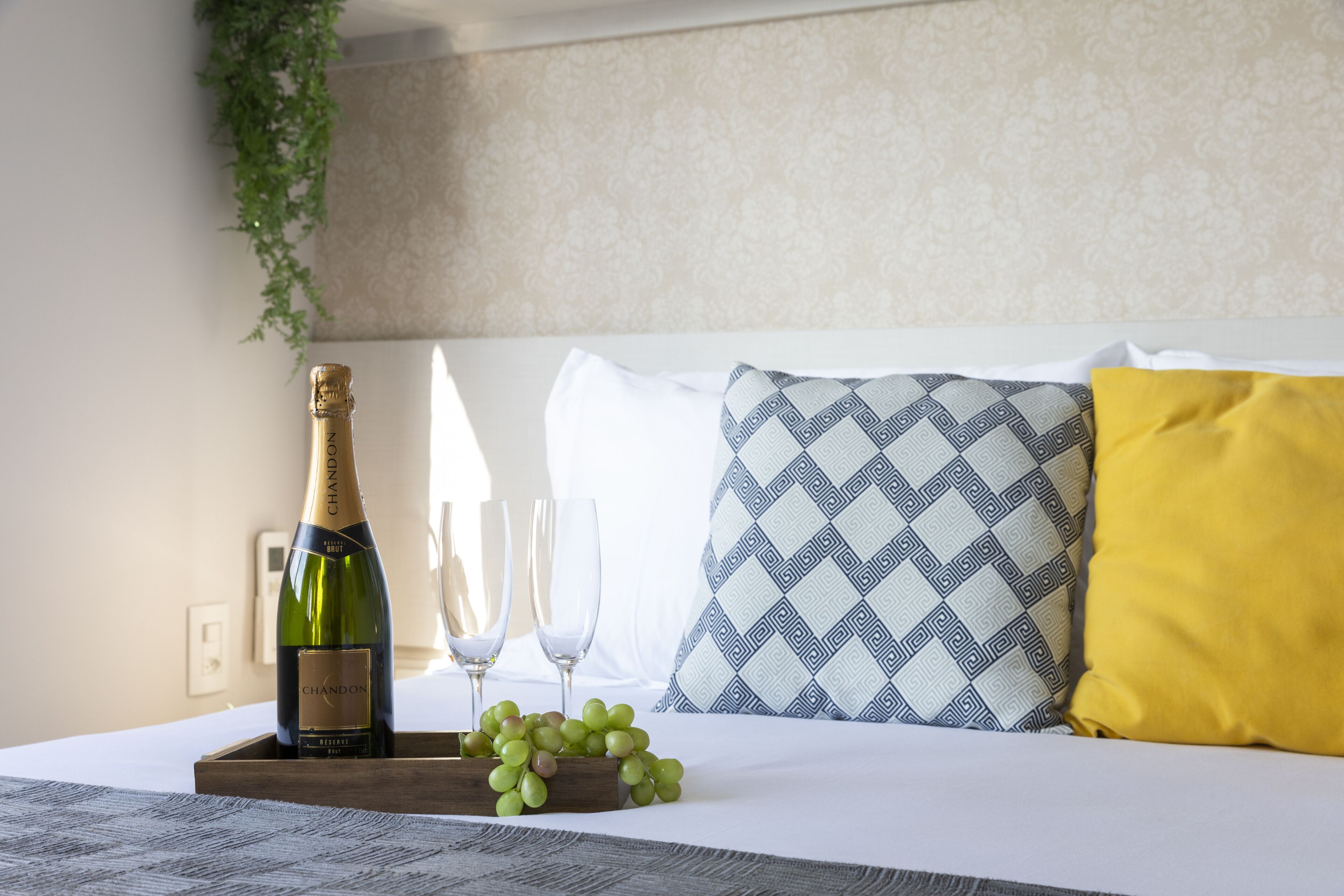 A bed with a bottle of champagne, two glasses, and a tray of grapes.