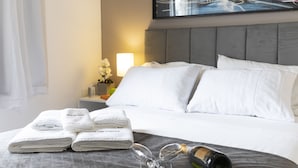 Habitación de hotel con una cama bien hecha, una mesita de noche con una lámpara y un cuadro con una vista urbana en la pared.
