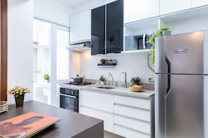 A modern kitchen with white cabinets, stainless steel appliances, a built-in microwave, and a refrigerator. - Thera Faria Lima (São Paulo)