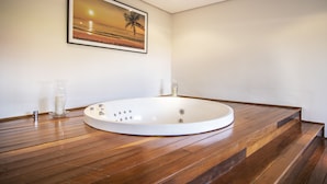 Un baño moderno con piso de madera, una bañera redonda y un cuadro enmarcado con una puesta de sol sobre el océano.