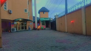 A courtyard with a paved ground, a building with a green awning, and a black gate. - Cameo's Suites (Lagos)