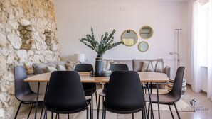 A modern living room with a stone wall, a wooden dining table, black chairs, a grey sofa, and a potted plant. - Seafront Duplex Living4malaga (Málaga)