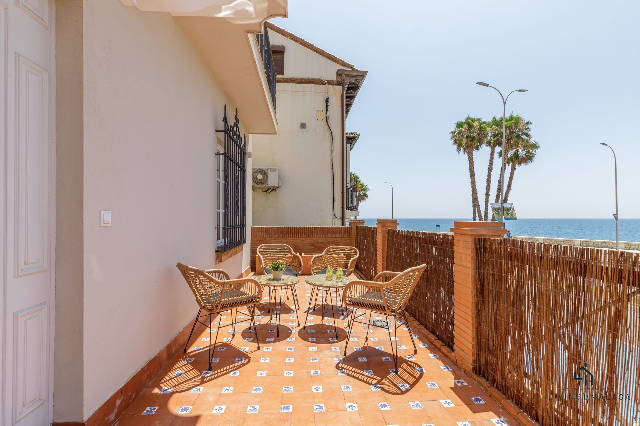 Een balkon met rieten meubilair, een betegelde vloer en uitzicht op zee.
