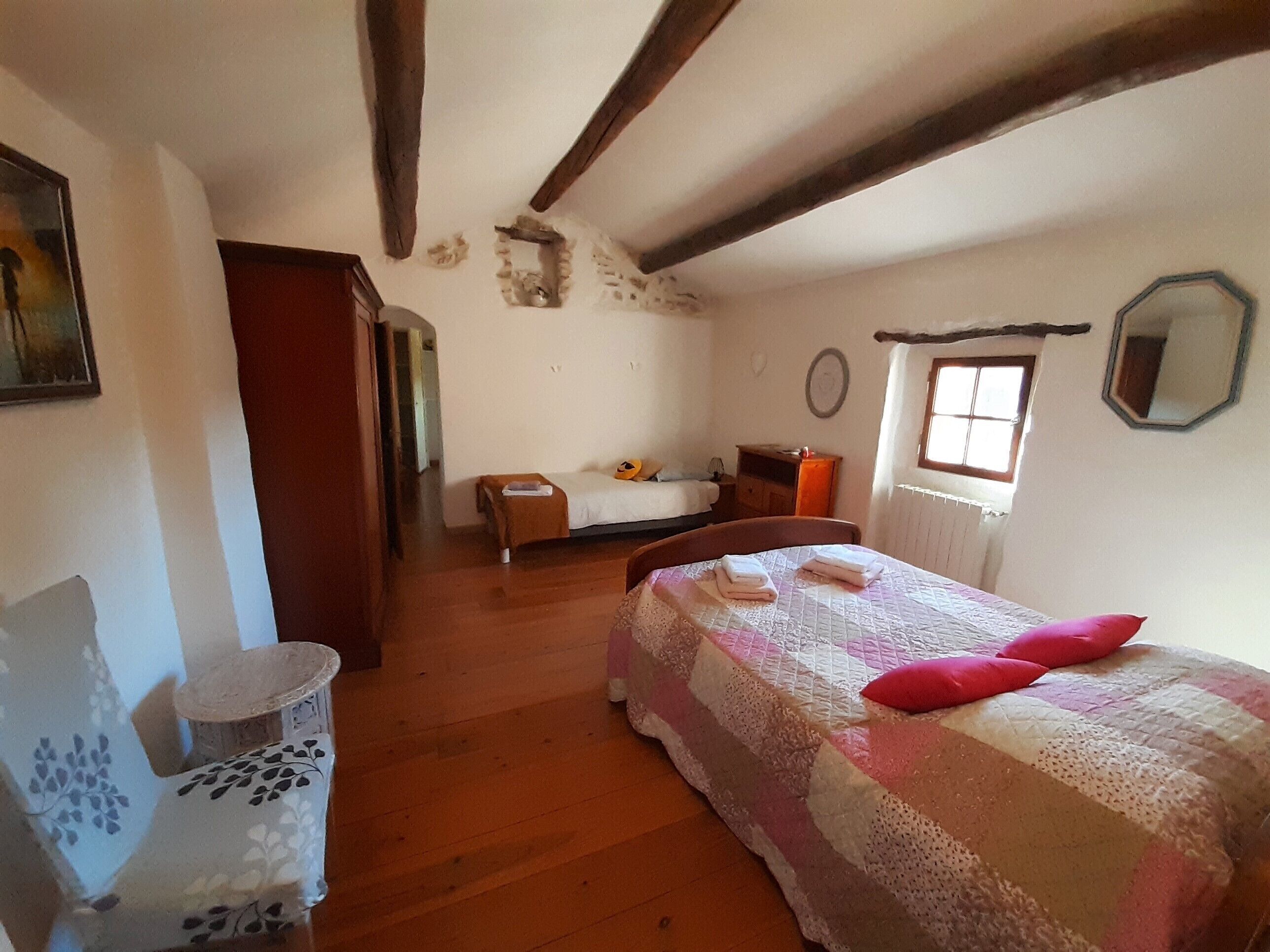 Quarto com piso de madeira, cama com colcha, cadeira, mesinha e espelho na parede.