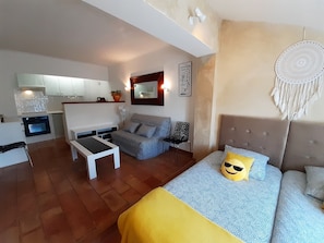 Um espaço compacto com cozinha compacta, sofá, cama com almofada decorativa e um sonho apanhador pendurado na parede.