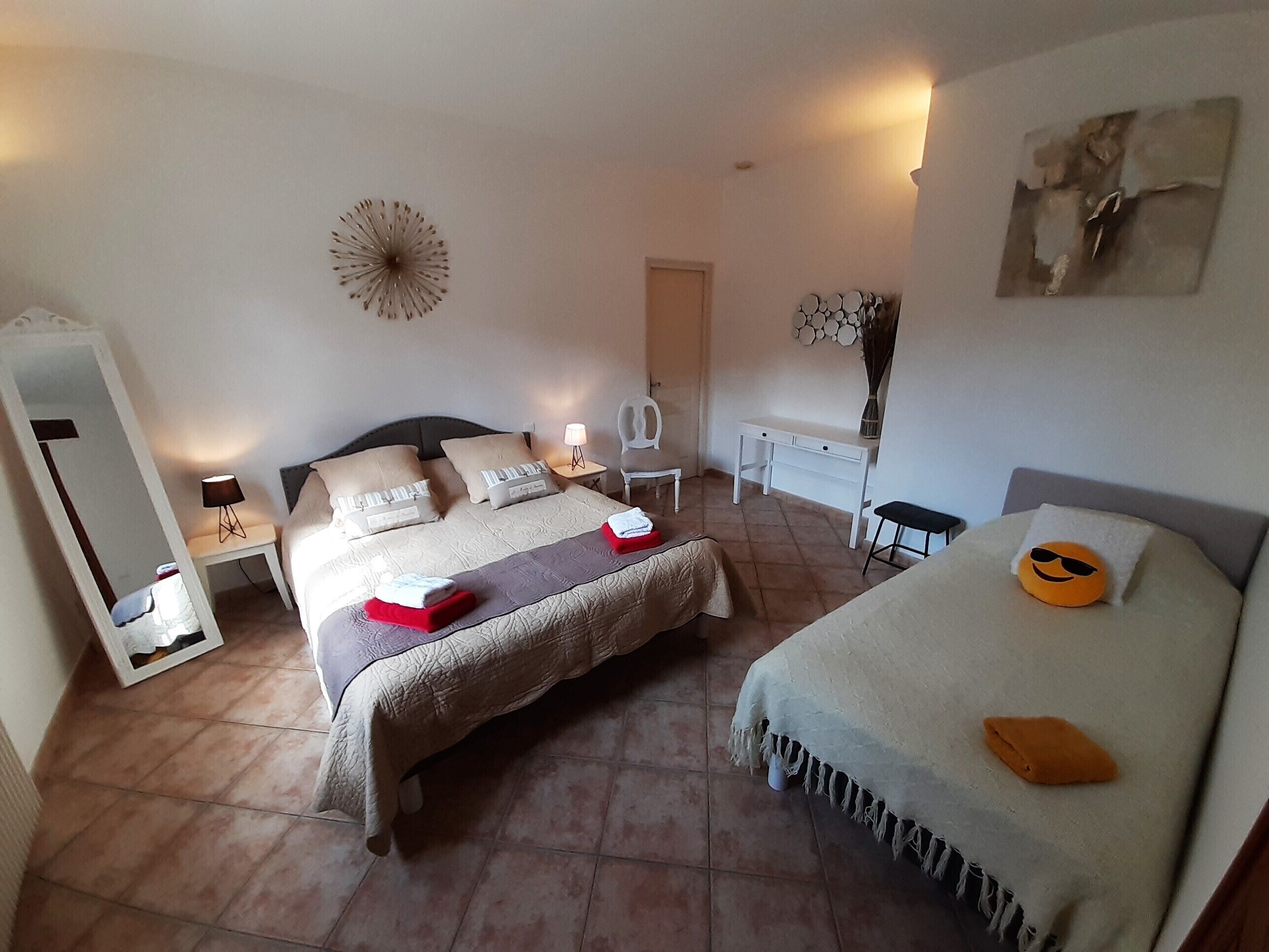 A hotel room with a bed, bedside tables, a chair, a desk, a mirror, and a wall decoration.