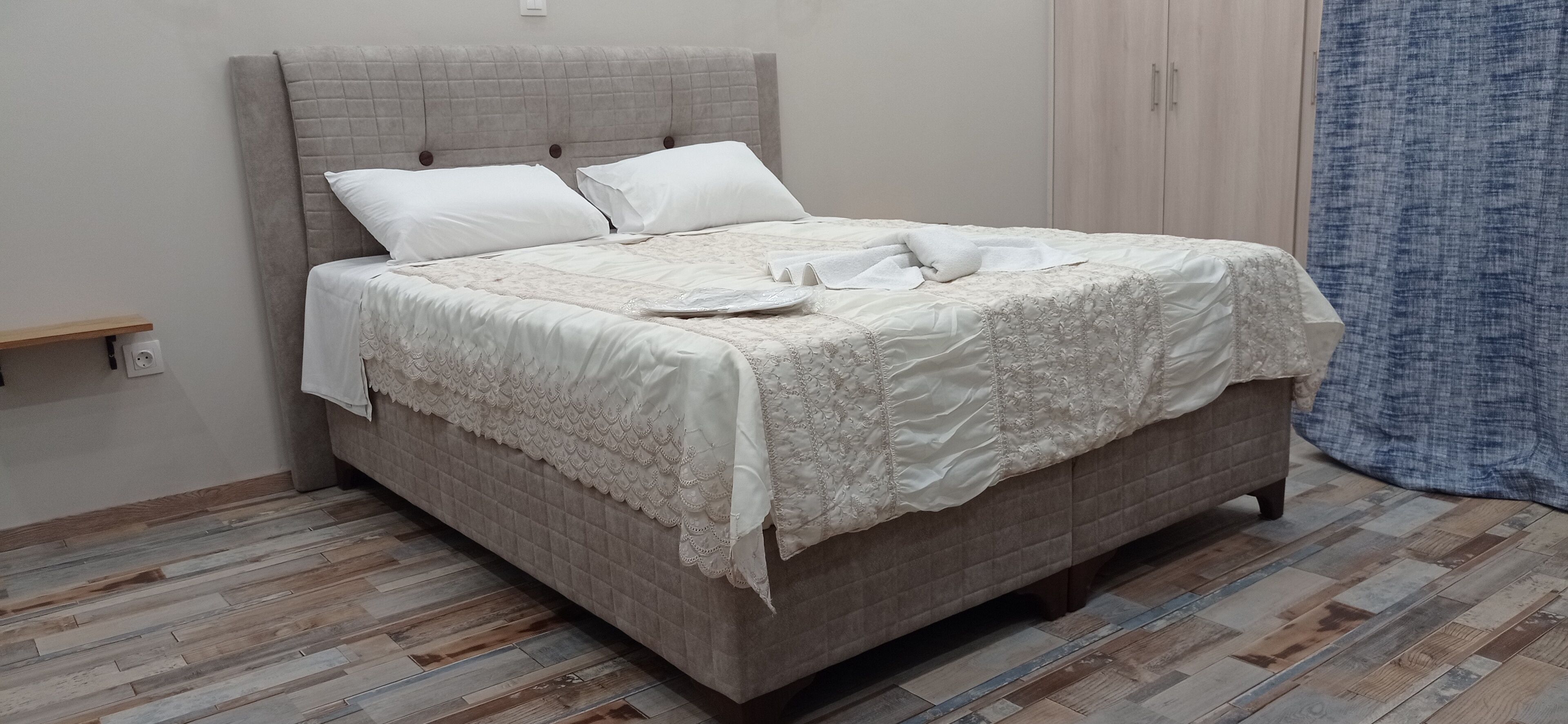 A neatly made bed with a quilted headboard and a wooden floor.