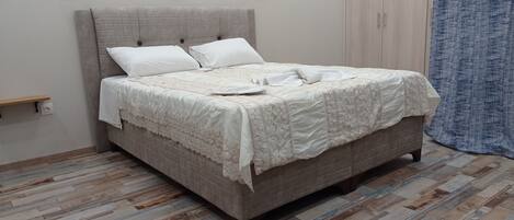 A neatly made bed with a quilted headboard and a wooden floor.