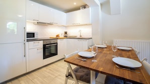 A modern kitchen with white cabinets, a wooden dining table set for two, and a built-in oven.