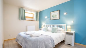 A bedroom with a bed, nightstands, a window with curtains, a radiator, and a framed picture on the wall.