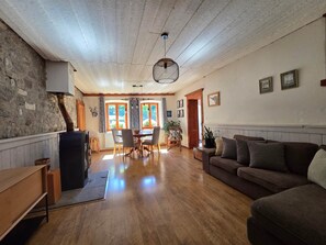 A spacious living room with a wooden floor, a dining area with a table and chairs, a sofa, and a fireplace.