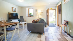 A living room with a sofa, a TV, a dining table with chairs, and a window with a plant.