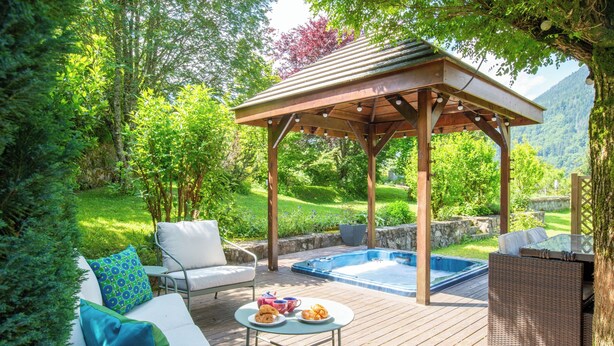 A wooden deck with outdoor furniture, a hot tub, and lush greenery.