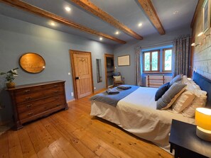 A bedroom with a wooden floor, a bed with pillows, a dresser, a wooden door, and a window with curtains.