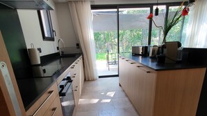 Une cuisine moderne dotée d’une porte-fenêtre coulissante donnant sur un balcon, d’une cuisinière encastrée et d’un plan de travail équipé de divers appareils électroménagers.