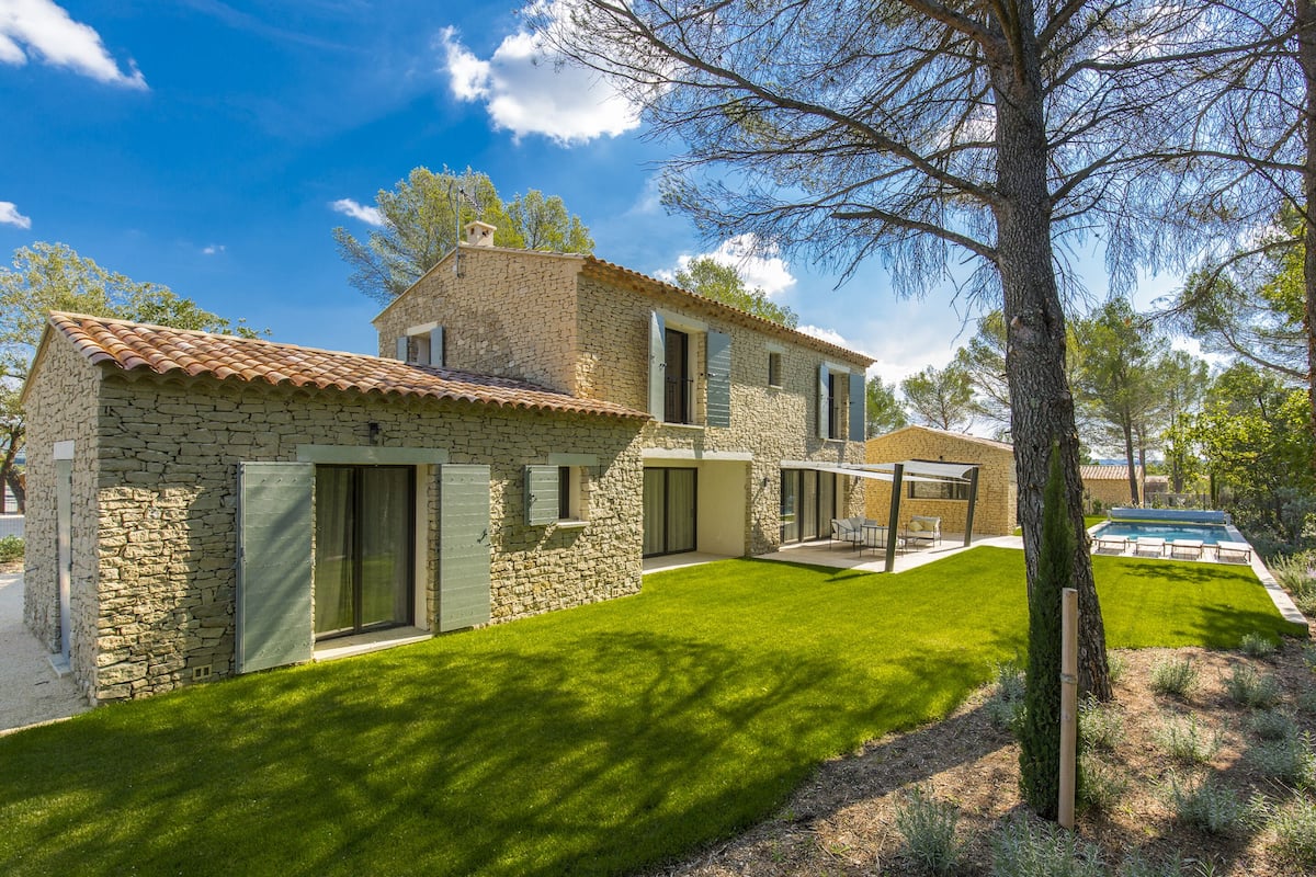 Una casa de piedra con techo de tejas, césped cuidado y piscina.