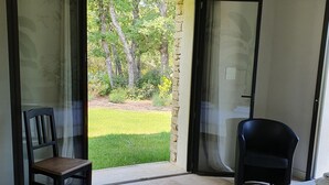 Une chambre avec un lit, une chaise et une vue sur un jardin, accessible par une porte-fenêtre coulissante.