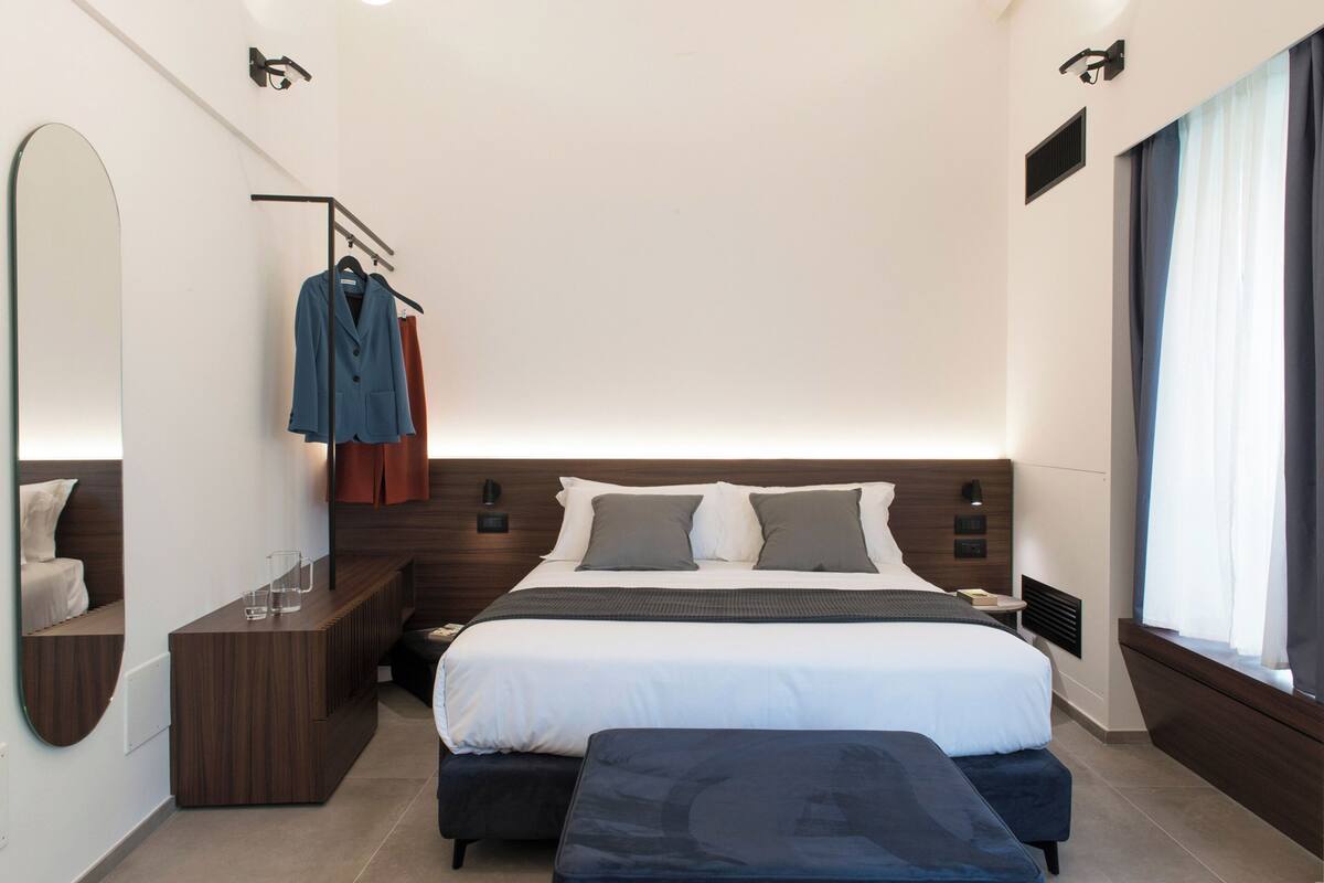 Una habitación de hotel moderna con una cama grande, mesitas de noche, un espejo y un armario.