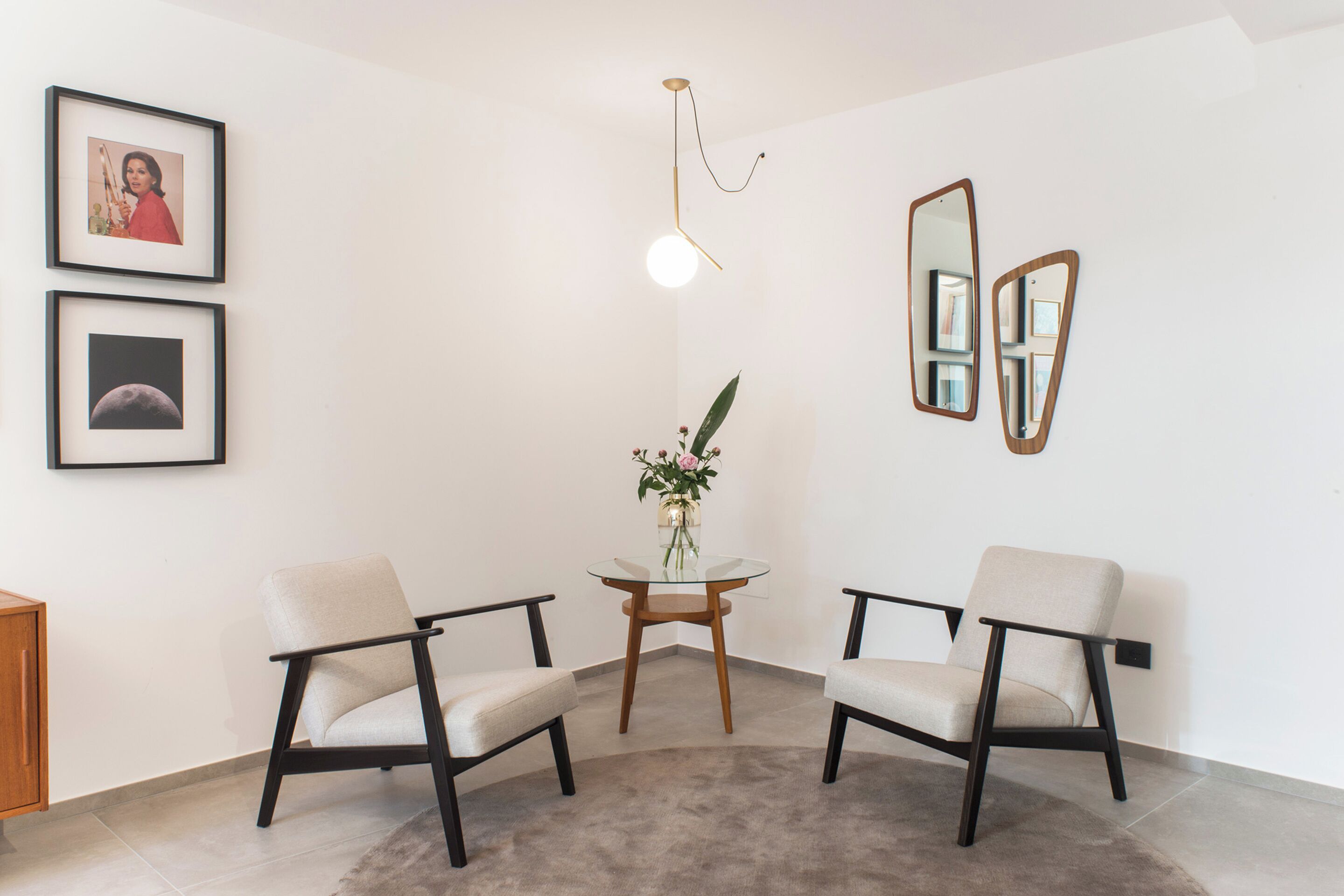 Een kamer met twee stoelen, een tafeltje met een vaas, ingekaderde foto's aan de muur en een bijzondere lamp.