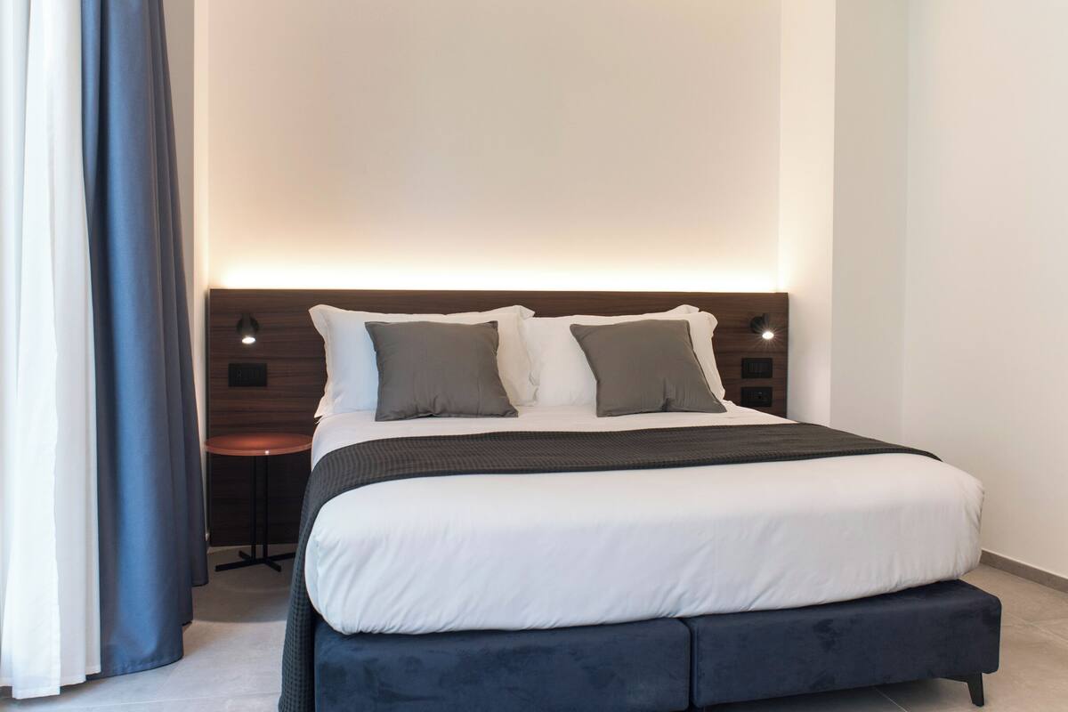 Una habitación de hotel moderna con una cama grande, una mesita de noche y una lámpara fijada a la pared.