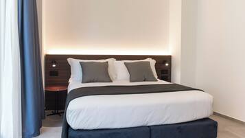 A modern hotel room with a large bed, a bedside table, and a wall-mounted light fixture.