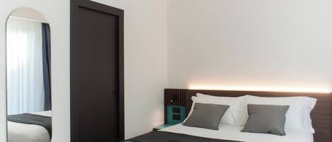 A modern hotel room with a large bed, a dark headboard, a bedside table, and a mirror.